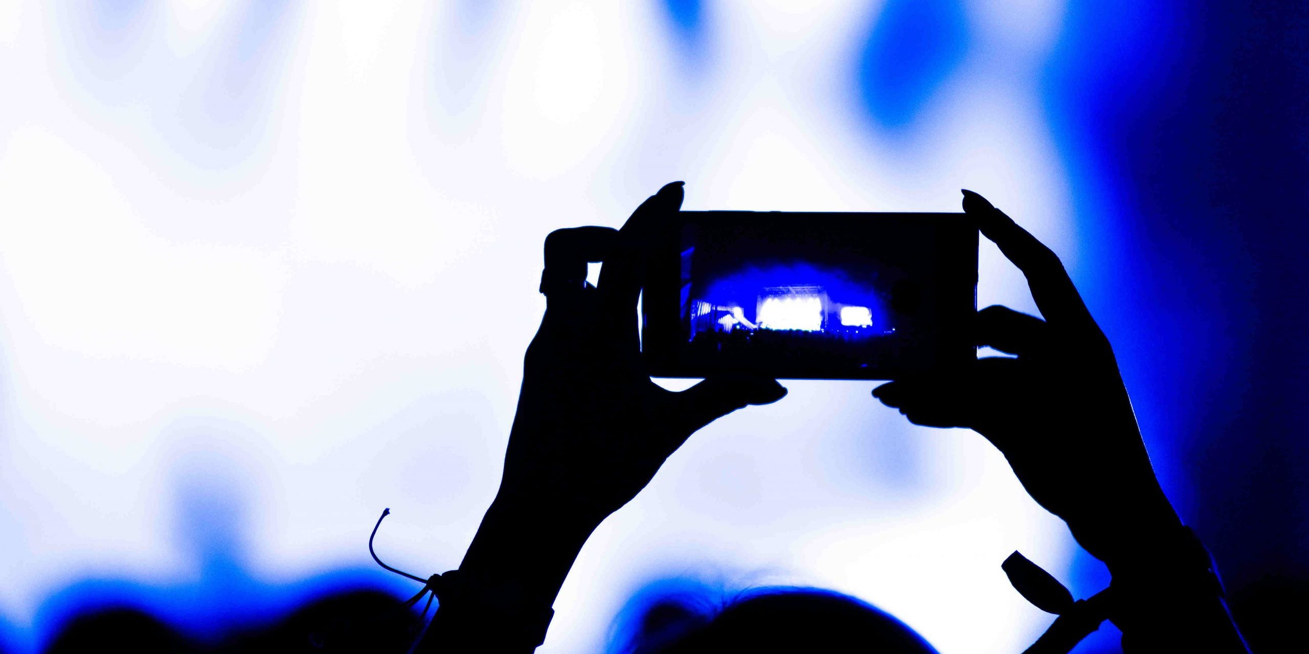 Silhouette of hands recording video with smart phone at music concert